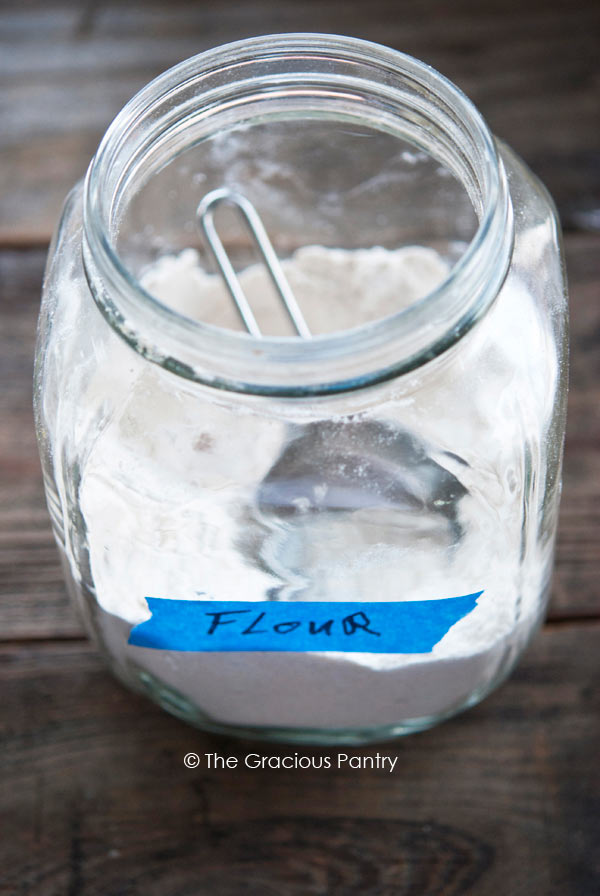 A large, glass canister partially filled with whole grain flour in Your Guide To Clean Eating Flour