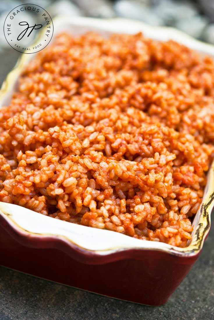 A small, dark red casserole dish is filled with Clean Eating Spanish Rice which is shown up close.