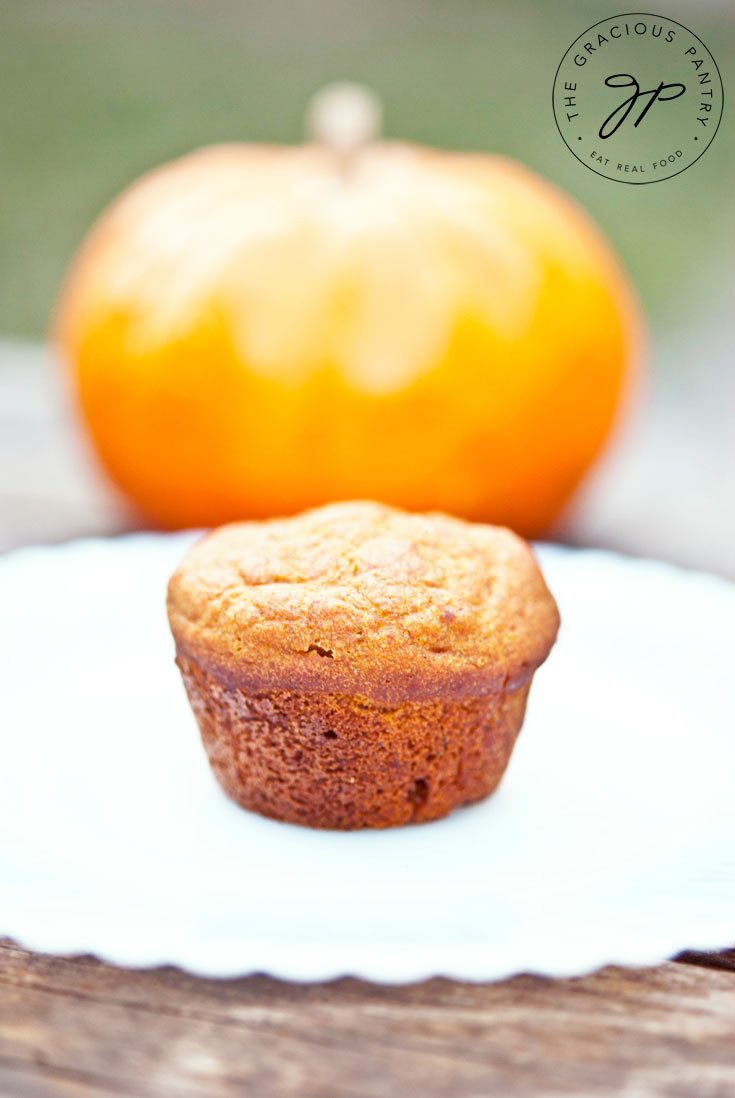 One from a big batch of Pumpkin Spice Mini Muffins sits on a white plate in front of a pumpkin.