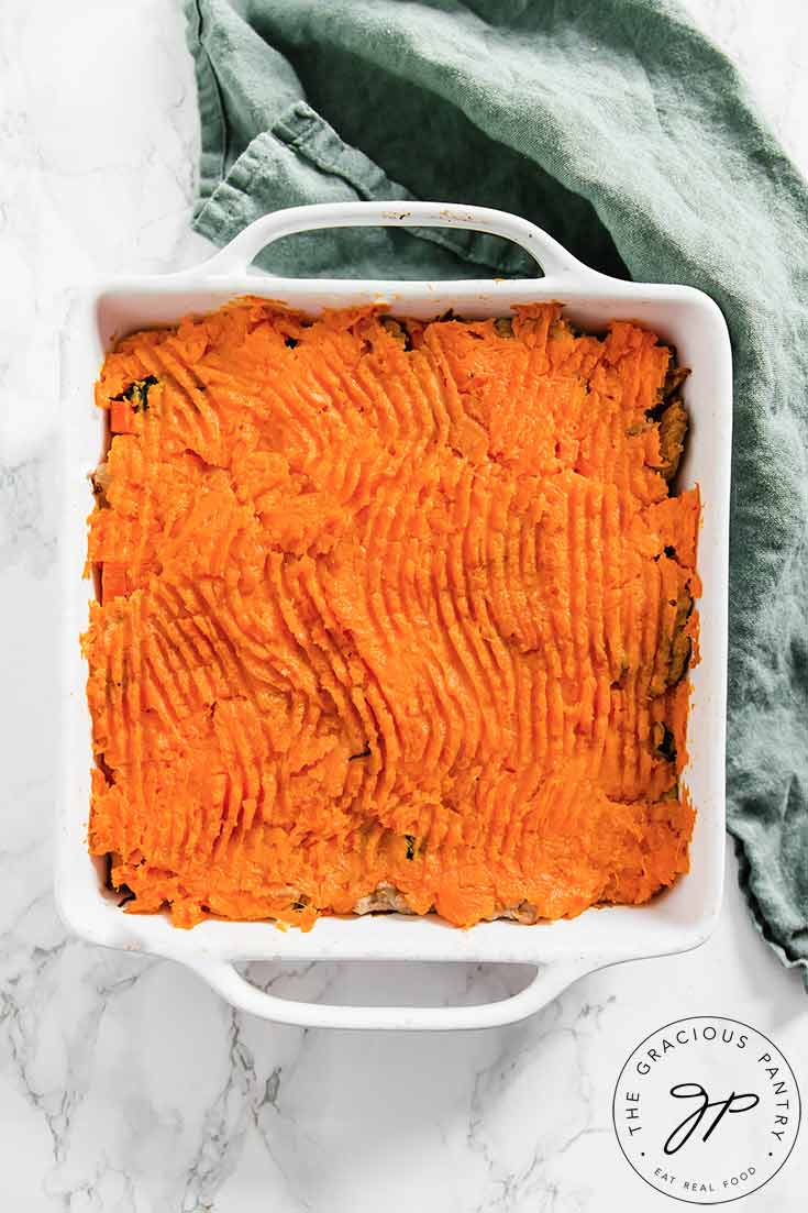 An overhead view of a white casserole dish sitting on a marble counter top with this just-baked Clean Eating Shepherds Pie cooling, untouched, in the dish.
