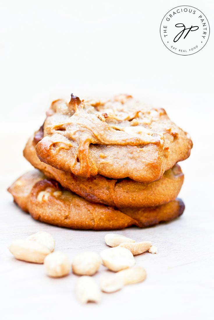 Three Clean Eating Peanut Butter Cookies sit on a white background, sticked one on top of the other.