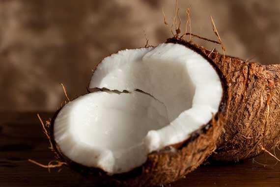 20 Clean Eating Recipes Made With Coconut Milk. Image depicts a cut open coconut with it's white flesh displayed in it's brown shell.
