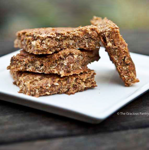 Clean Eating Coconut Lime Oat Bars displayed on a white plate. There are three square bars stacked up with a forth leaning against them sideways.