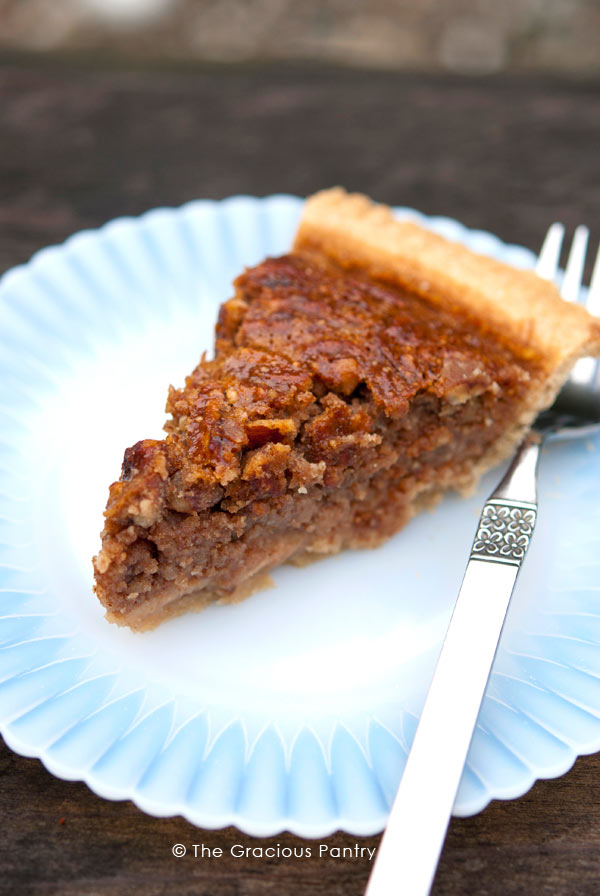 A single slice of Pecan Pie on a white plate with a fork resting next to it.