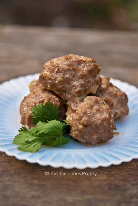 Clean Eating Garlic Parmesan Turkey Meatballs piled on a small, white plate and garnished with some greens.