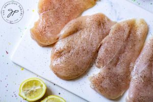 Step one of this lemon caper chicken recipe shows the raw chicken breasts sitting on a cutting board, ready to prep.