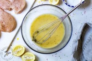 Step two shows the whisked lemon sauce in a mixing bowl with the whisk still in it. Cut lemons sit to the side of the bowl.