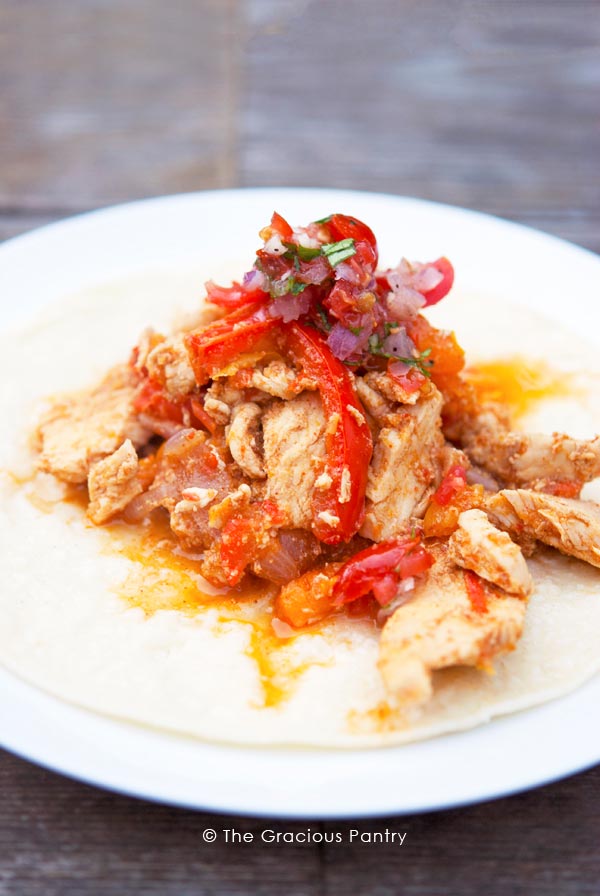 A single plate of Clean Eating Fajitas Recipe. It shows a single fajita, open on the plate. You can see the chicken and peppers piled on top of the open tortilla.