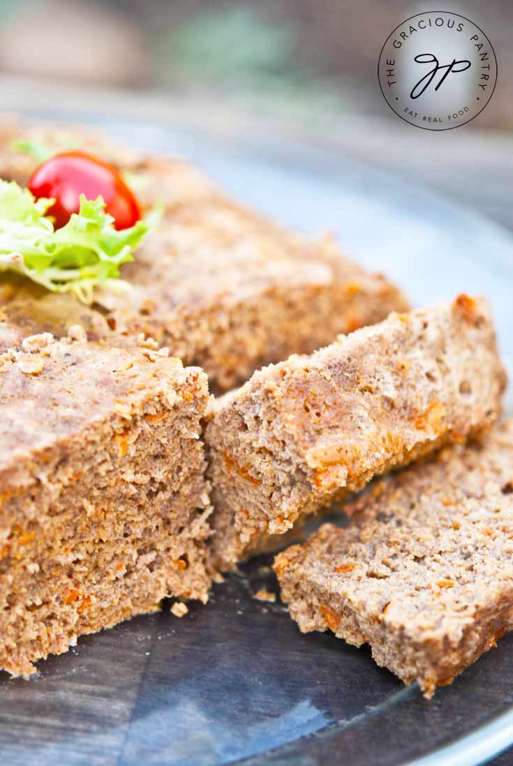 Clean Eating Slow Cooker Meatloaf sitting on a platter and shown up close. It has a few slices off the front that are laying nicely on the platter in front of the loaf.