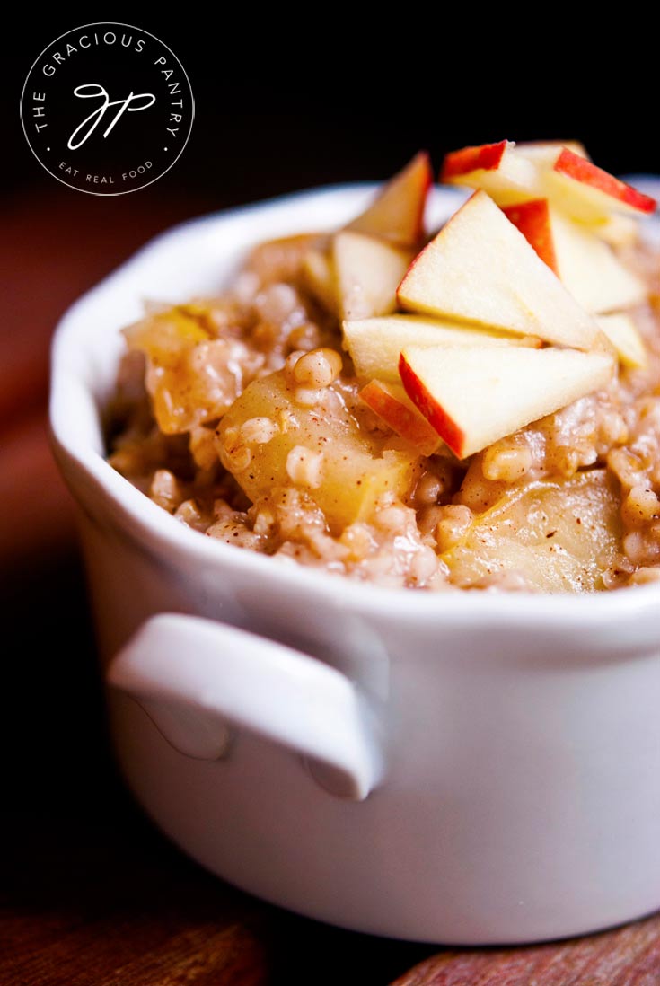 A closeup shot of this Clean Eating Apple Pie Oatmeal in a white bowl with fresh cut apples on top for garnish.