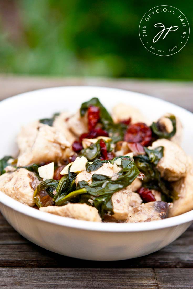 Clean Eating Coconut Almond Cranberry Chicken in a white bowl, shown up close. You see the chances of chicken, the red cranberries and plenty of spinach.