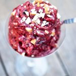 A clear martini glass sits on a wooden surface, filled with Cherry Nice Cream and topped with chopped walnuts.