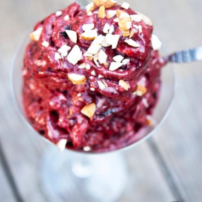 A clear martini glass sits on a wooden surface, filled with Cherry Nice Cream and topped with chopped walnuts.