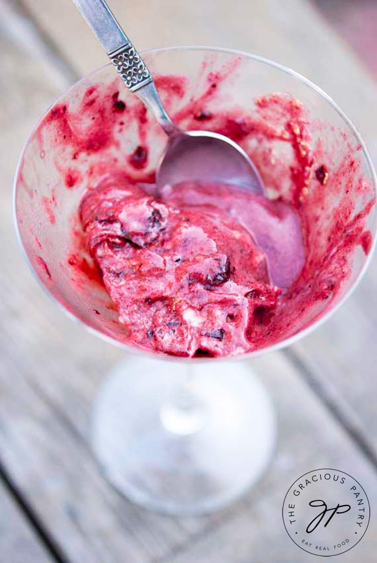 A clear martini glass shows this Clean Eating Cherry Almond Ice Cream more than half eaten with a spoon still sitting in the the glass.