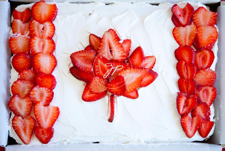 A view of this Clean Eating Canada Day Cake from overhead, looking down. The Canadian flag design is made from sliced, red strawberries placed over white cake frosting.