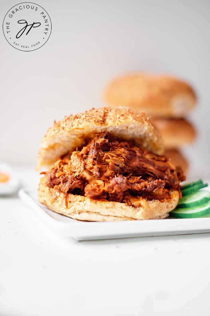 Pulled Pork Sandwiches with one on a plate with sliced cucumbers on the side.