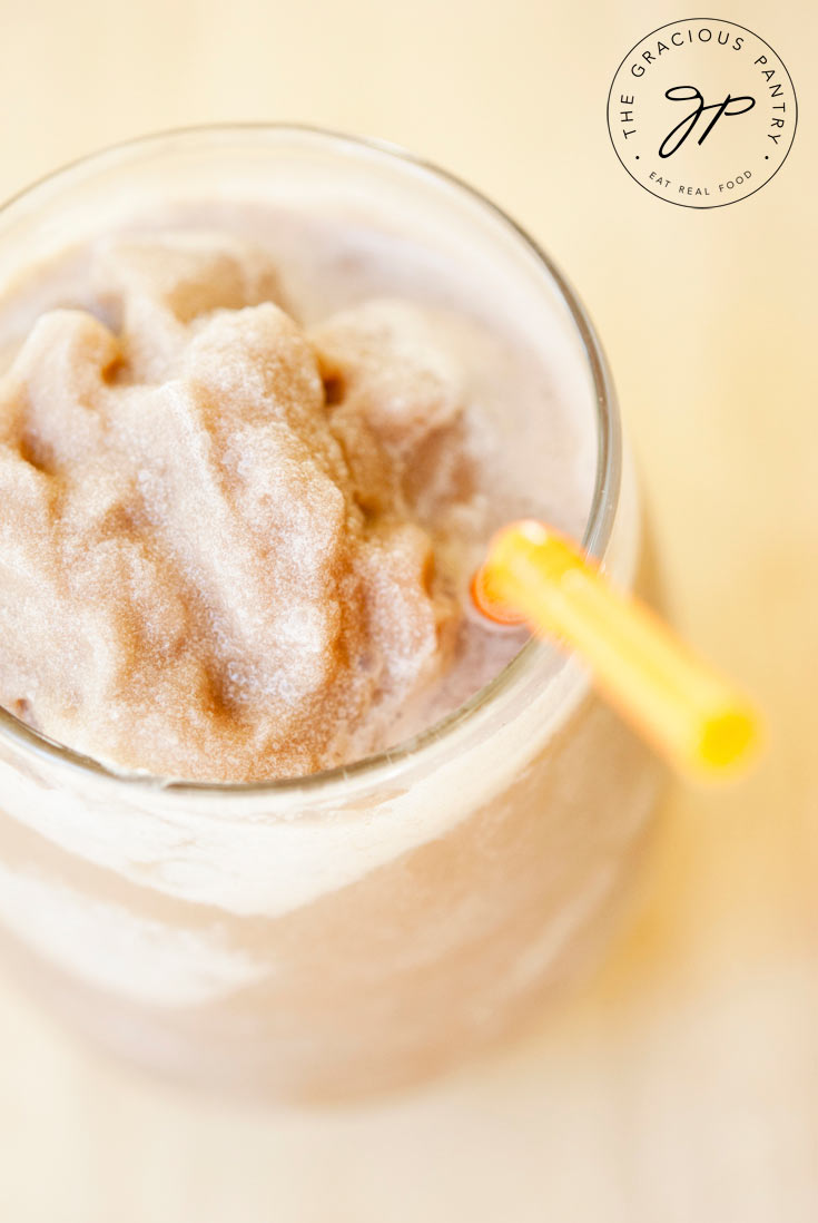 Image shows a clear glass filled with this Clean Eating Mocha Coconut Frappuccino. It has a light colored, coffee-brown icy or slushy appearance.