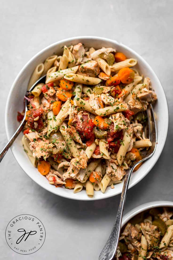 A close up view of a single while bowl containing this Clean Eating Slow Cooker Pork Ragout. It has two spoons on either side of the bowl, ready to serve this bowl of deliciousness.