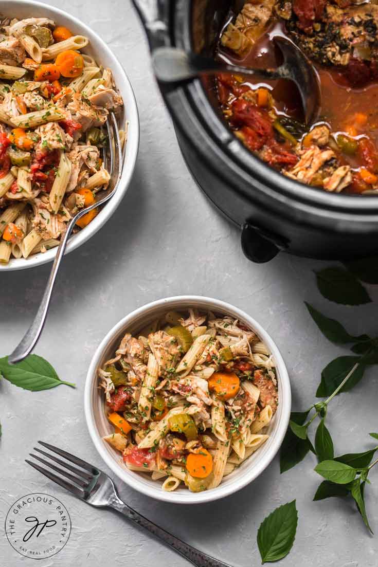 This Clean Eating Slow Cooker Pork Ragout has just been served. The bowls of food are still sitting next to the slow cooker and both white dishes are full and ready to serve.