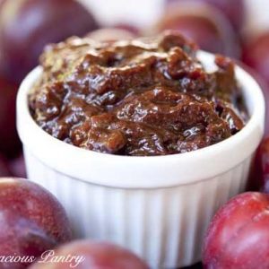 Plum Butter in a white bowl surrounded by fresh plums.