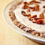 A partial view of the whole ice cream pie. You can see the layer of crust, the ice cream and the pecan pieces topping it.
