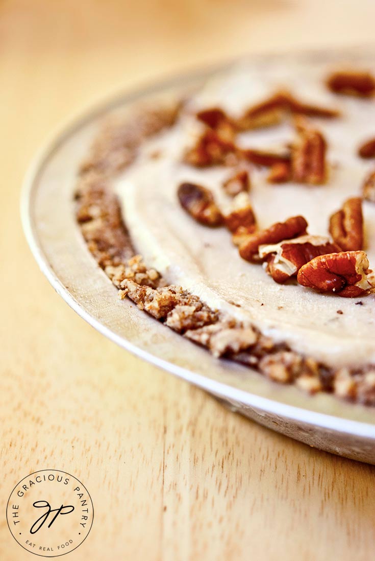 A partial view of the whole ice cream pie. You can see the layer of crust, the ice cream and the pecan pieces topping it.