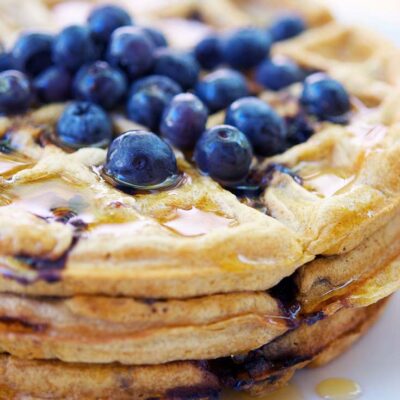 Blueberry waffles stacked on top of each other with fresh blueberries sprinkled over the top.