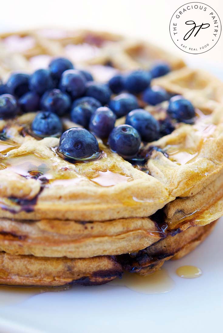 Blueberry waffles stacked on top of each other with fresh blueberries sprinkled over the top.