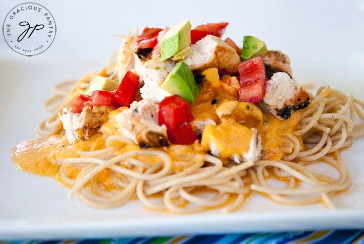 A side view of this Chicken Alfredo Pasta shows the pasta, sauce, chicken and toppings such as tomatoes and avocado.