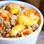 A white bowl sits on a wood surface filled with curry pineapple turkey rice bowl.