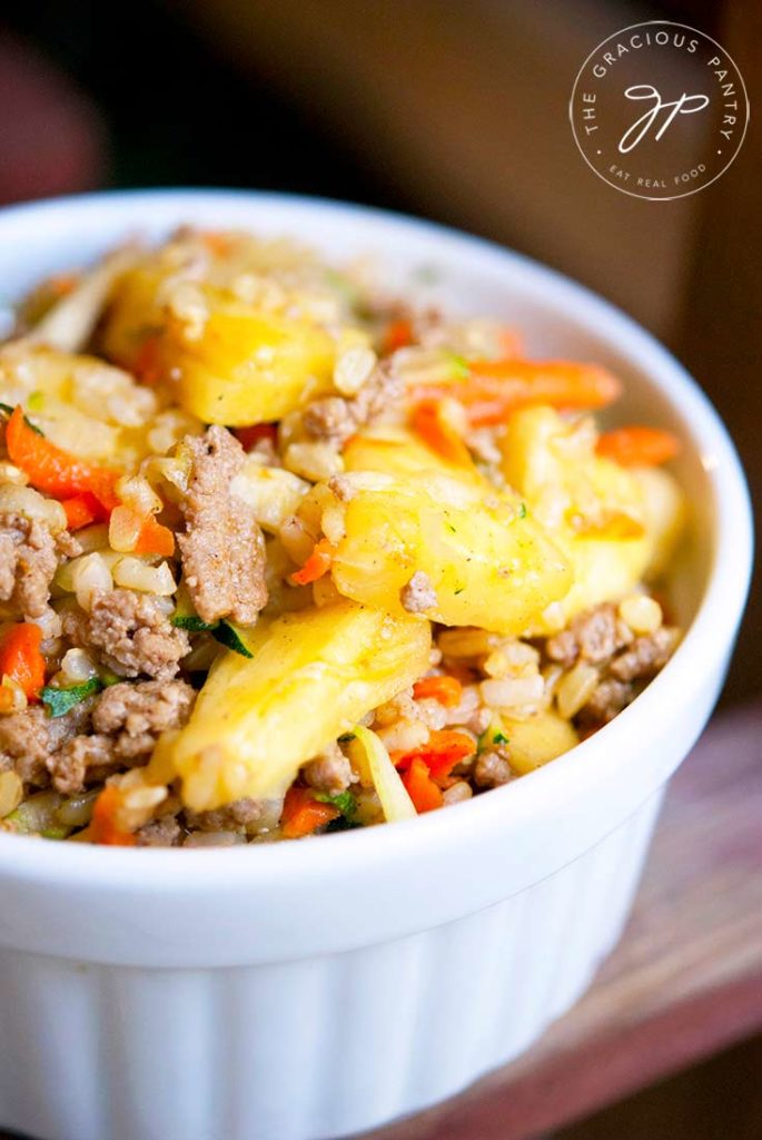 A white bowl sits on a wood surface filled with curry pineapple turkey rice bowl.