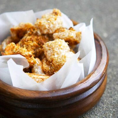 A wooden bowl with a parchment liner sits filled with golden brown popcorn shrimp.