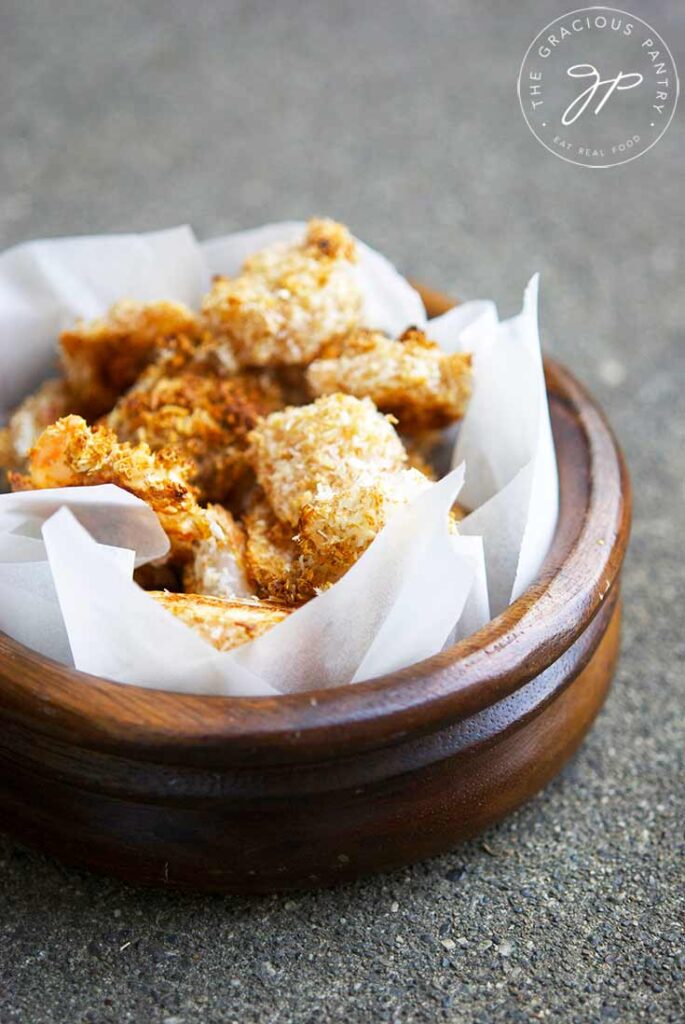 A wooden bowl with a parchment liner sits filled with golden brown popcorn shrimp.