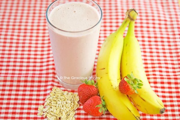 A straight on photo of this Clean Eating Strawberry Oatmeal Smoothie Recipe with bananas, strawberries and raw oats gathered around the glass.