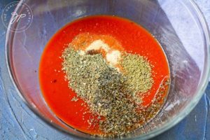 Combining the tomato sauce and spices in a mixing bowl.