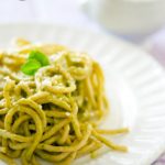 A white plate sits on a purple-checkered tablecloth. The plate is piled high with a twirl of pasta covered in thei clean eating avocado pest sauce recipe.