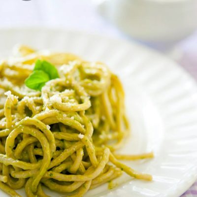 A white plate sits on a purple-checkered tablecloth. The plate is piled high with a twirl of pasta covered in thei clean eating avocado pest sauce recipe.