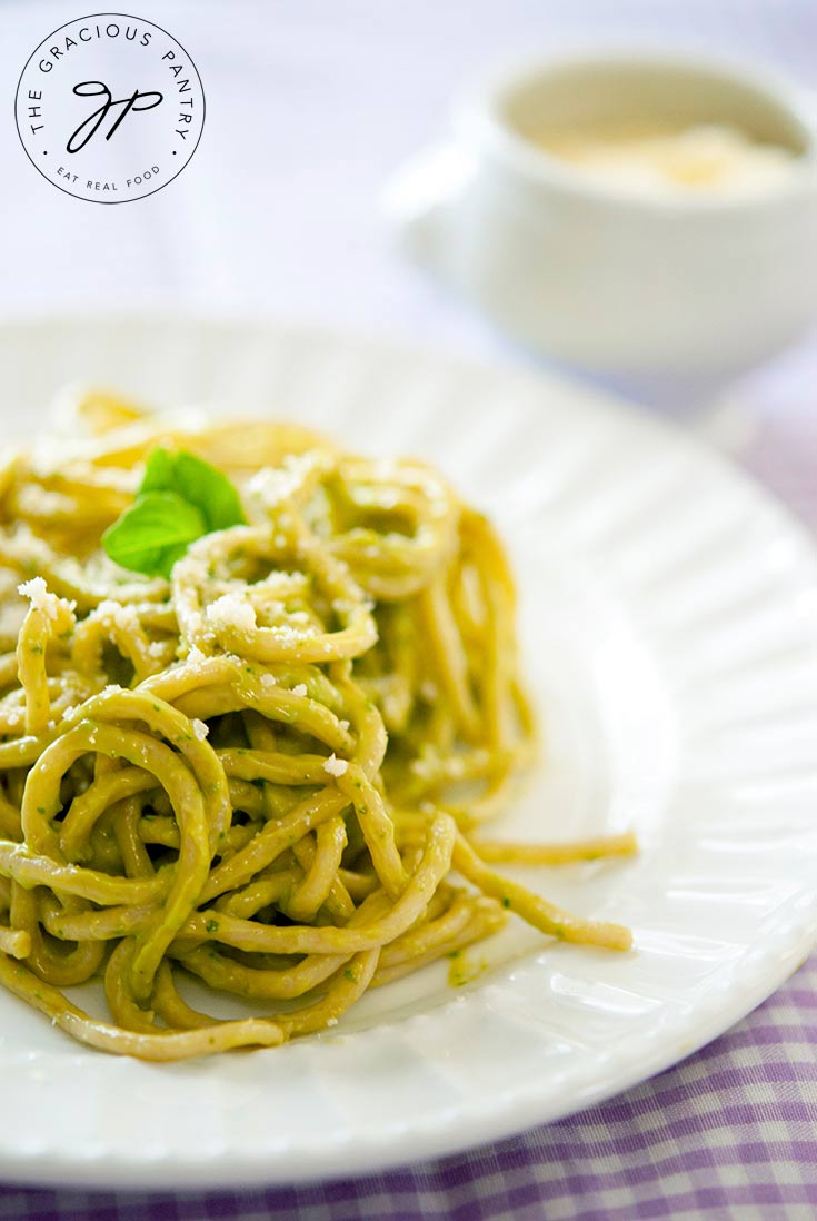 A white plate sits on a purple-checkered tablecloth. The plate is piled high with a twirl of pasta covered in thei clean eating avocado pest sauce recipe.