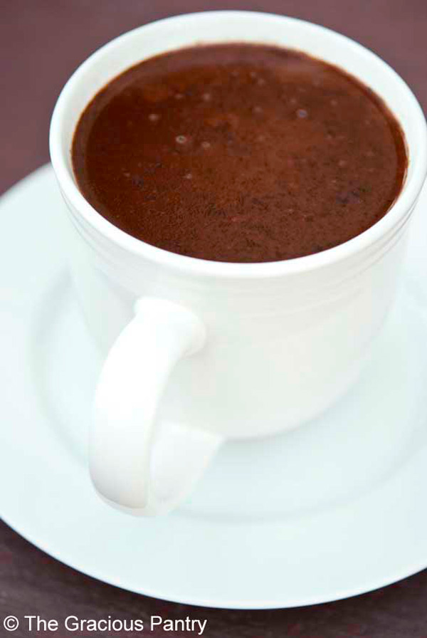 A close up shot of a white mug sitting on a white saucer filled with this Clean Eating Coconut Hot Chocolate.