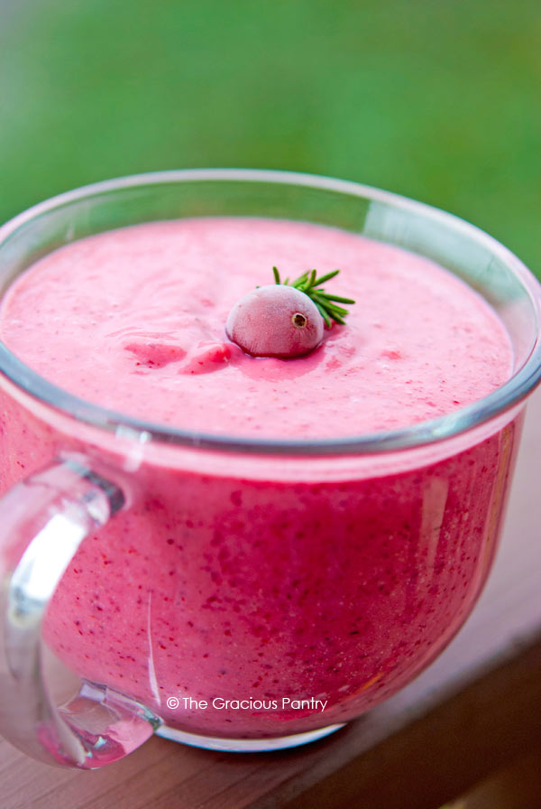 Clean Eating Cranberry Banana Smoothie shown in a clear mug, up close. The smoothie is a bright pink color with a single cranberry floating on top.