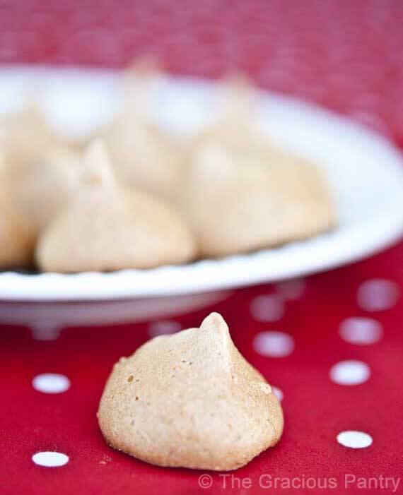 A white plate of Clean Eating Meringue Cookies sits on a red and white, polka dot table cloth. In front of the plate sits a single meringue.