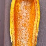 Half a baked delicata squash sits on a wooden plank, slightly golden brown from the oven and ready to eat.