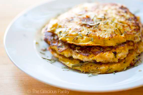 Three cauliflower fritters sit on a white plate, garnished with dry herbs.