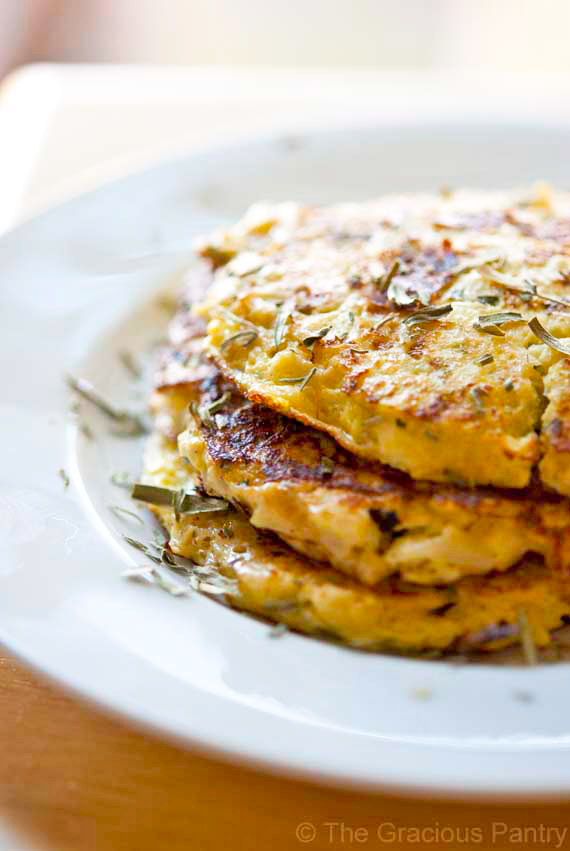 A white plate with three Cauliflower Fritters sticked on top of each other. Dried herbs garnish the plate and fritters.