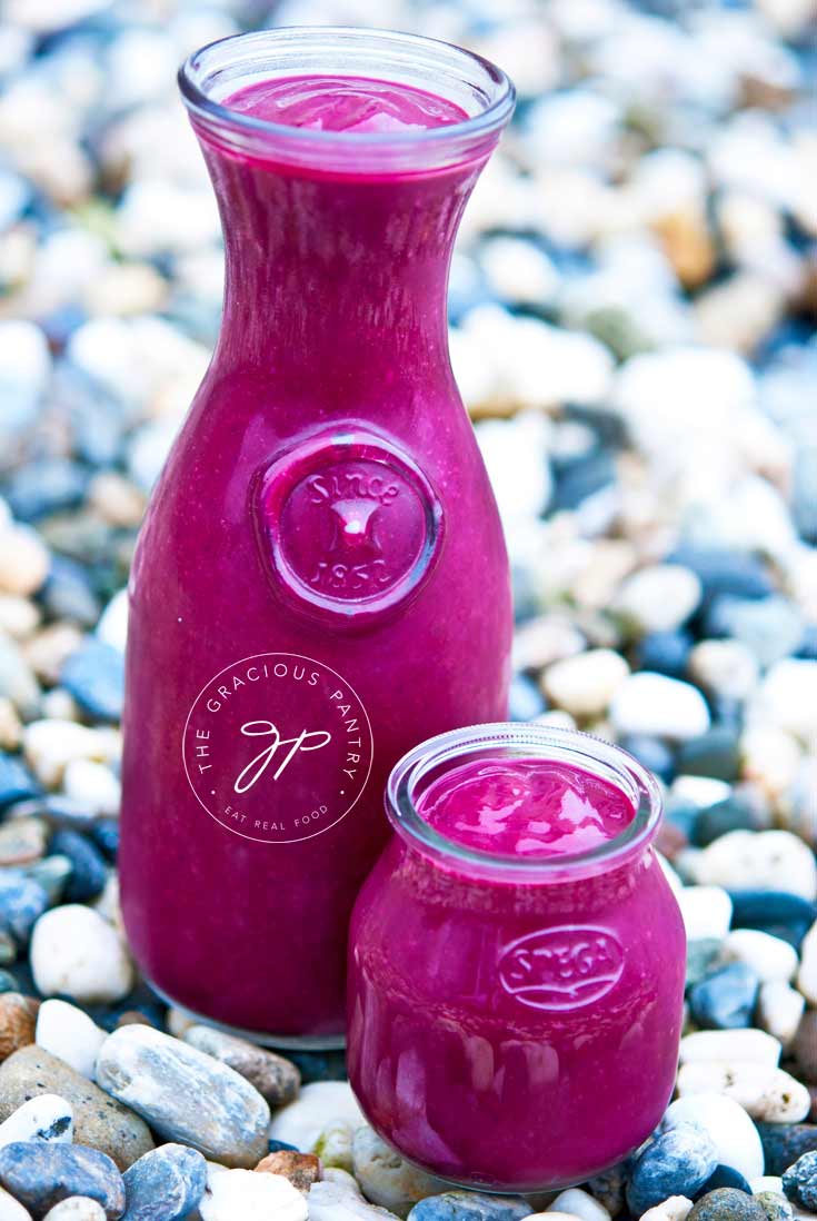 2 glass jars of Clean Eating Cherry Beet Smoothie sitting on multi-colored pebbles. One jar is a taller carafe and the other is a small, short, single serving jar.