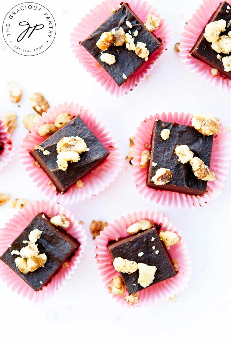 An overhead shot looking down at many pieces of Clean Eating Banana Walnut Fudge. There are pieces of walnuts sprinkled over the top and each piece sits in it's own, red, cupcake paper.