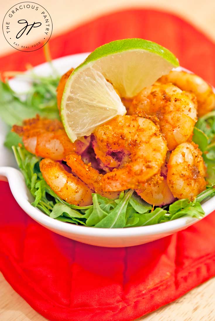 Taco Shrimp piled high in a white bowl on a bed of leafy greens and a twisted slice of lime placed on top for garnish.