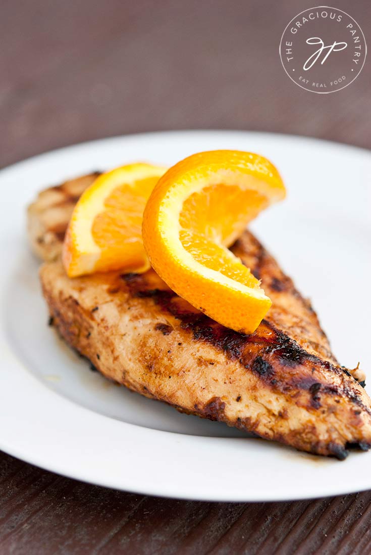 Clean Eating Citrus Grilled Chicken breast served on white plate with a slice of orange twisted and placed on top for garnish.