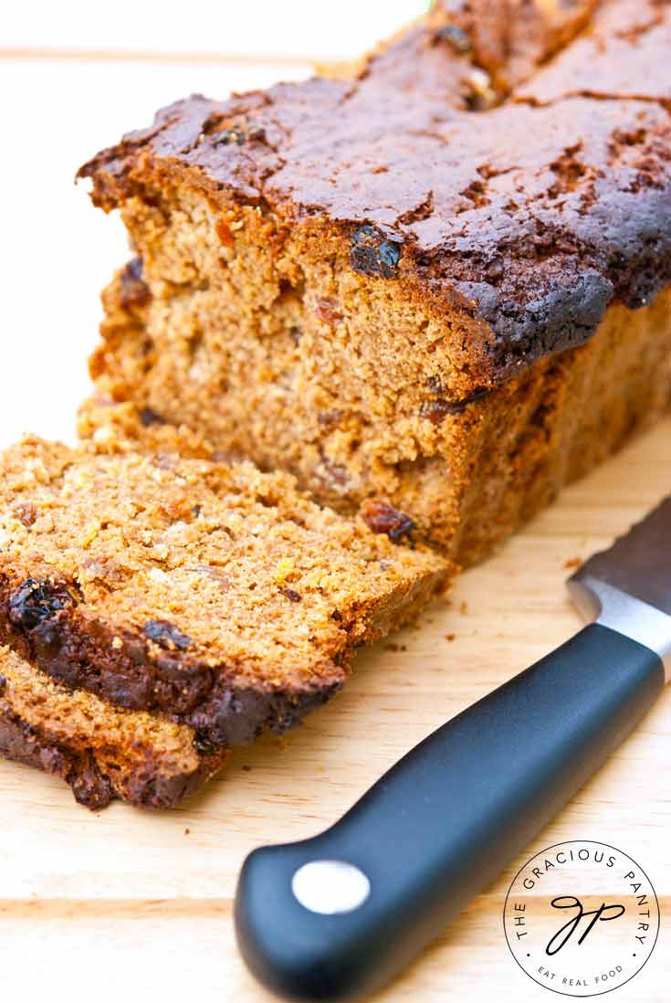 A loaf of this Clean Eating Irish Spice Bread sits on a cutting board with a knife laying next to it. A single slice has been cut off and lays in front of the loaf.