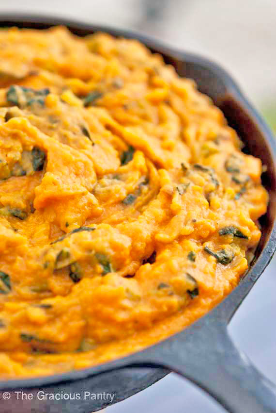 An up close view of this Clean Eating Irish Colcannon in a black, cast iron pan. You can see bits of dark green from the kale mixed in with the bright orange sweet potatoes.